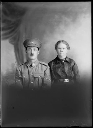 Studio upper torso unidentified family portrait, a Lance Corporal World War I soldier with toothbrush moustache, [Tui or Huia?] collar and hat badges and wife in black lace blouse with brooch, Christchurch