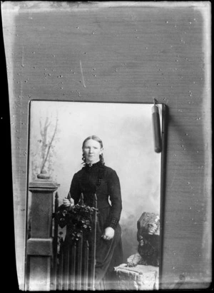 Studio portrait of an unidentified woman, standing behind a gate, possibly Christchurch district