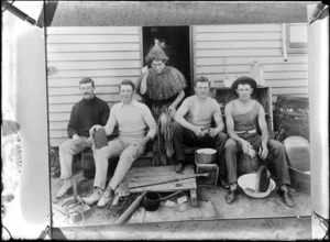 Unidentified group of men performing domestic chores outdoors, including cleaning dishes and peeling potatoes, also includes a man dressed in Maori costume holding a knife, probably Christchurch district
