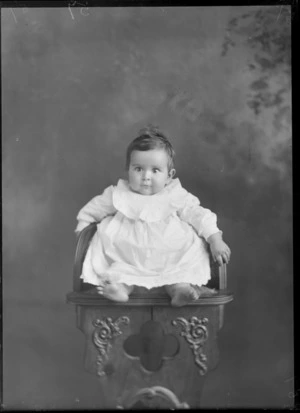 Studio portrait of unidentified baby, sitting in a carved wooden chair, probably Christchurch district