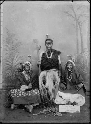 Group of three unidentified men in 'native' costume, with painted faces and a painted studio background, also includes a sign reading 'Lulu, Guide to Pastry Eruption', probably Christchurch district
