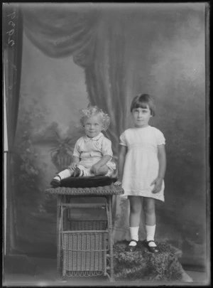 Studio unidentified family portrait of a young girl standing next to her toddler sister sitting on a cane table, Christchurch