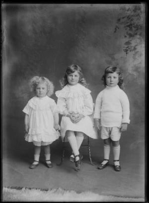 Studio unidentified family portrait of three young sisters, two in lace dresses with large collars, a third in a woollen jersey, with the oldest sitting, Christchurch