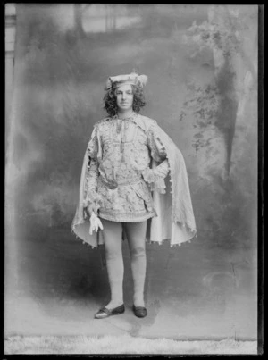 Studio portrait of an unidentified young man dresses up in historical costume as a court nobleman or herald of the middle ages with a patterned tunic, cape and cap, Christchurch