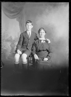 Studio unidentified family portrait, mother in pin striped jacket and shorts, shirt and tie with school socks sitting, Christchurch