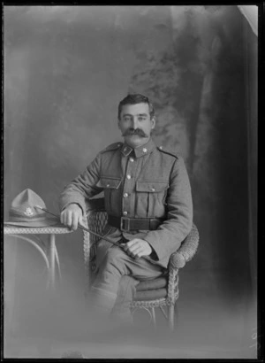 Studio unidentified portrait of a World War I soldier sitting with large handlebar moustache, star collar [Army Service Corps?] and hat [Reinforcements?] badges and swagger stick, Christchurch