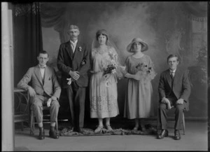 Studio unidentified wedding party, groom with a large moustache and bride with a long veil standing with two men and a bridesmaid with a hat, women holding flowers, Christchurch