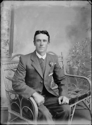 Studio unidentified wedding portrait, groom in a three piece pin striped suit with a carnation sitting on a couch, Christchurch