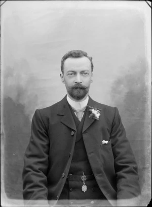 Studio upper torso portrait of unidentified man with a beard, chequered tie, waistcoat pendant and carnation, Christchurch