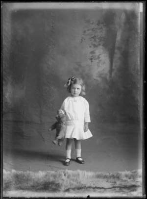 Studio portrait of an unidentified small girl holding a teddy bear, possibly Christchurch district