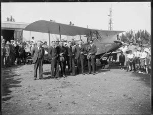 Biplane outside hanger with a group of men in front, crowd looking on, sign saying 'flights 10 shillings & 6 pence'on hanger door