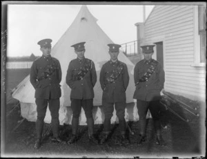 Four unidentified soldiers wearing cartridge belts, standing in front of a tent, at casual camp, Hastings