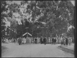Crowds of people gather to look at the Maori exhibits at the carnival, Hastings, showing a meeting house and waharoa (Maori Gateway)