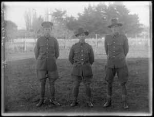 Three unidentified officers standing to attention in a field, at casual camp, Hastings