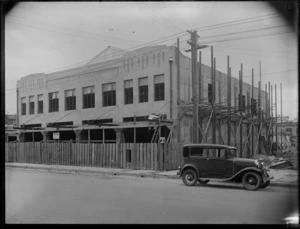 An unidentified man working on a construction site, Hastings, with a motor car in front of the building