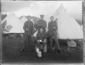 Four unidentified soldiers, three standing and one sitting on a wooden crate holding a tin plate, cup, utensils and an ABC tin in front of the tent, at casual camp, Hastings