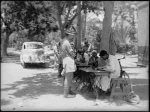Native tailors in the street of Maadi village make minor alterations to the uniforms of New Zealanders from the nearby camp, World War II - Photograph taken by G Kaye