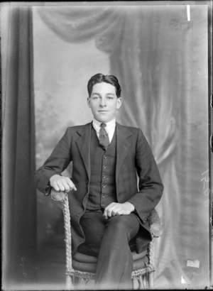 Studio portrait of unidentified young man in a pin striped three piece suit with necktie pins sitting in a cane chair, Christchurch
