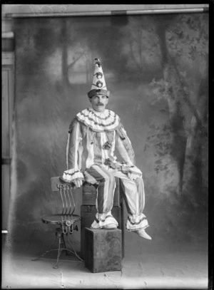 Studio portrait of an unidentified man in dress up costume, wearing a striped clown suit, with three pompoms down the middle of his pointed hat, possibly Christchurch district