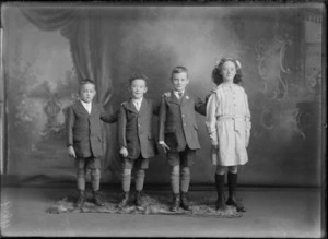 Studio portrait of members of an unidentified family, showing the three boys dressed in identical short suits, with a white shirt and tie, long woollen socks with ankle boots, with the girl wearing a cotton dress, with a ribbon in her hair, long woollen socks with ankle boots, possibly Christchurch district