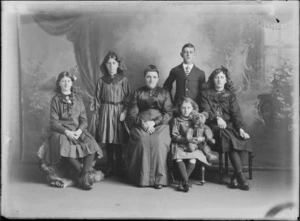 Studio unidentified family portrait of an older mother with her four daughters in dark large collar dresses with brooches and bows, bracelets, wrist watch and teddy bear, and son with striped school tie, Christchurch