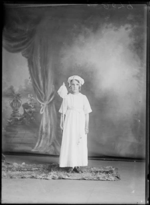 Studio unidentified portrait of a young girl in a costume, a white cotton dress with a pearl belt, sleeve and collar edging, a cloth hat with pearl necklaces holding a pole with a cotton handkerchief, Christchurch