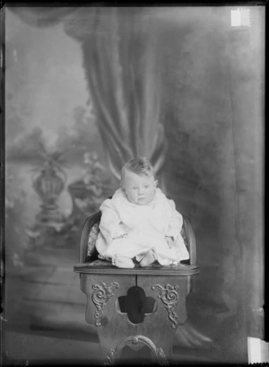 Studio unidentified family portrait of baby in a lace petticoat and cotton dress, sitting on a wooden highchair, Christchurch