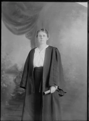 Studio portrait of an unidentified young woman wearing an academic gown, and holding a rolled up document, possibly Christchurch district