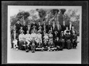 Outdoor on a tennis court, a group portrait of thirty three unidentified men and women with hats and a baby, with three schoolboys in uniform and teenaged girl in front, probably Christchurch region