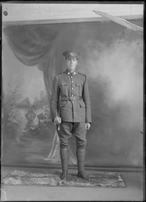 Studio unidentified portrait of a World War I young soldier with collar and hat badges, with black shoulder pocket cord, holding a swagger stick standing, Christchurch