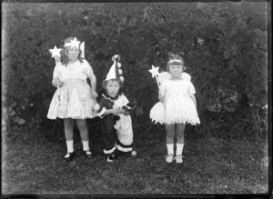Outdoors portrait of two unidentified young girls in fairy costumes and a younger boy dressed as a clown, probably Christchurch region