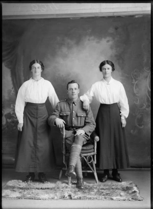 Studio portrait of unidentified World War I soldier with 'Liverpool' collar badges, sitting between two women with pearl necklace and bar brooch, Christchurch