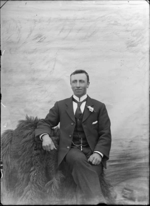 Studio portrait of unidentified man with a stiff Imperial shirt collar, patterned tie and buttonhole and a pocket watch chain greenstone pendant, probably Christchurch region