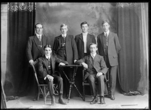 Studio portrait of unidentified bicycle road racing team, with four young men in suits, manager with polka dot tie and coach alongside, Christchurch