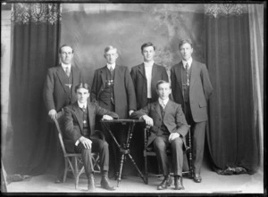 Studio portrait of unidentified bicycle road racing team, with four young men in suits, manager with polka dot tie and coach alongside, Christchurch