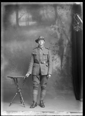 Studio portrait of unidentified World War I soldier with slouch hat, collar and hat badges, standing with stirrups and riding crop in hand [Mounted Rifles?], Christchurch