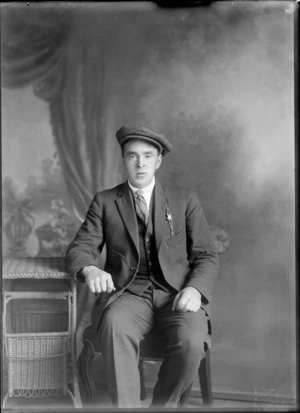 Studio portrait of an unidentified man sitting in cloth cap and three piece suit, striped shirt and plaid tie, with pocket watch lapel chain with pendant, Christchurch