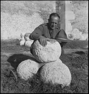 L Ballantyne with large round stones used as missiles by defenders of ancient fortress of Lucera, Italy, World War II - Photograph taken by George Kaye