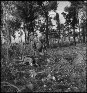 NZ infantry soldiers pass dead German soldier during attack on German HQ at Castelfrentano, Italy, World War II - Photograph taken by George Kaye