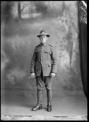 Studio portrait of unidentified young World War One soldier and hat with white band and badge, standing with riding crop in hand, wearing putties and stirrups [Mounted Rifles?], Christchurch