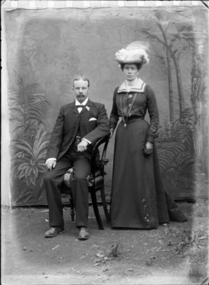 Unidentified couple outdoors, with a painted backdrop behind, probably Christchurch district