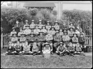 Outdoors in a park area with wooden building behind, group portrait of the Saint Saviour's Boy Scouts Troop, with boys and adults in scout uniforms with an Anglican Priest, bugle, drum and English flag, with 30th October 1920 sign in front, Christchurch