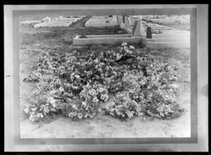 Unidentified cemetery, view of an unmarked grave covered in flowers, with grave plots with headstones beyond, probably Christchurch region