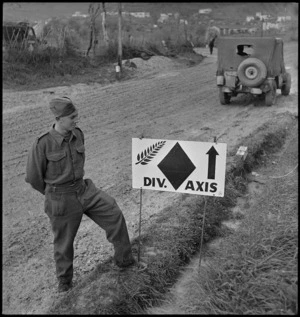 J B Woodward stands beside signpost indicating the line of advance of the NZ Division in Italy, World War II - Photograph taken by George Kaye