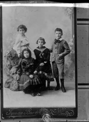 Studio family portrait of four unidentified young children, two girls in sailor shirts with dresses, and boy and girl with large bow tie - original photograph by Tynan Brothers, 41 Bath Street, Jersey, UK.