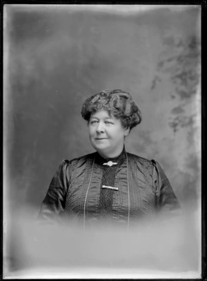 Studio upper torso portrait of an unidentified older woman in a dark lace neck and front blouse with coin and greenstone bar brooches, Christchurch