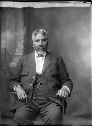 Seated studio portrait of a man [Mr Wakarua?] wearing a suit, tie and a watch chain with a pounamu pendant attached [Kapeu, ear pendant?], Christchurch
