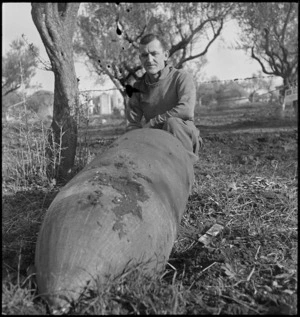 W Hanley alongside bomb that landed near house occupied by New Zealanders and rolled into an olive grove, Italy, World War II - Photograph taken by George Kaye