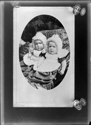 Viquetted portrait of unidentified [twin?] babies, outdoors, dressed in identical clothing, including bonnets, probably Christchurch district