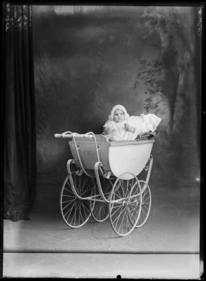 Studio family portrait of unidentified baby in a large wooden pram wearing a bonnet, Christchurch